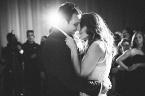 A bride and groom share an intimate first dance at their Resort at Pelican Hill wedding reception, surrounded by guests in a dimly lit venue.