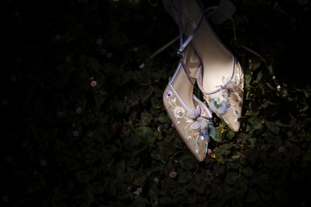 At a Nestldown wedding, a pair of beige high-heeled shoes with floral embroidery is placed on a leafy, dark green ground.
