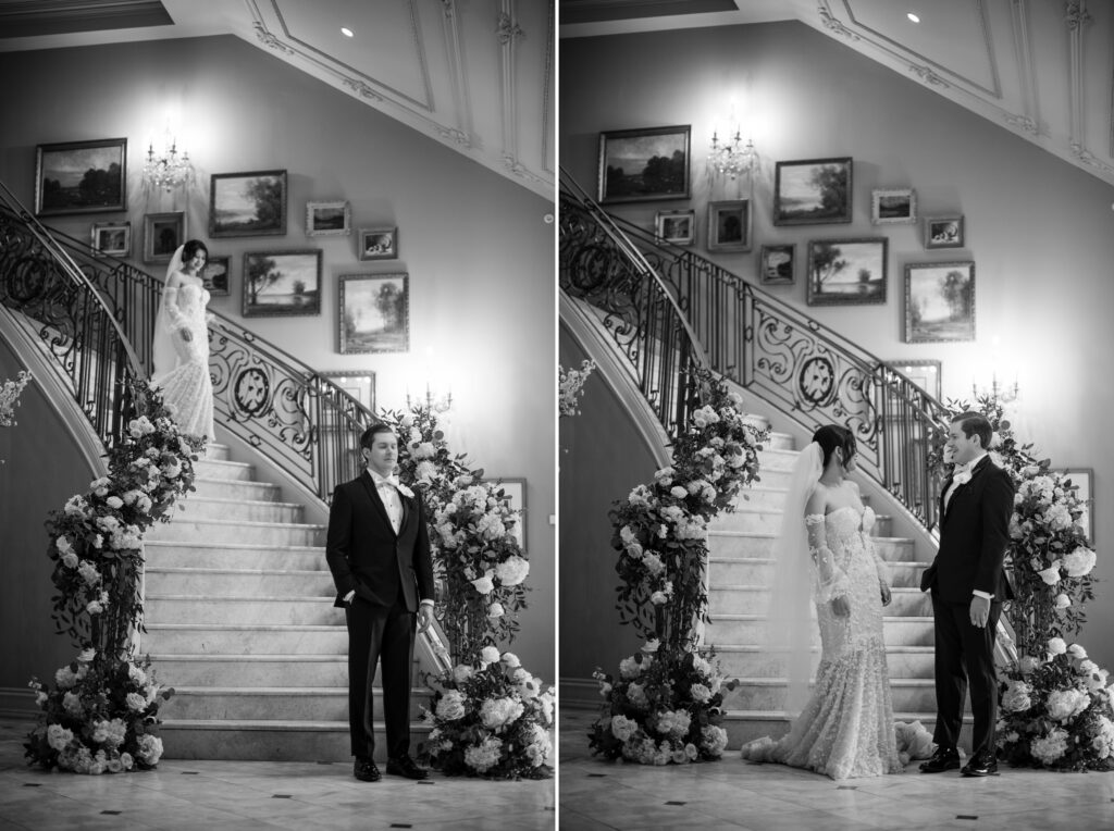 At a Park Chateau wedding, the bride and groom stand on an elegant staircase adorned with flowers; the bride is ascending while the groom awaits her at the base in a black and white ambiance, capturing their first look.