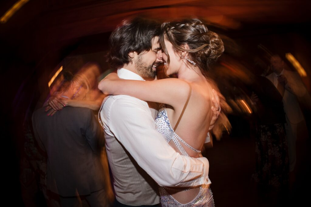 A couple embraces and dances closely at a Nestldown wedding, with blurred figures and warm lighting in the background.