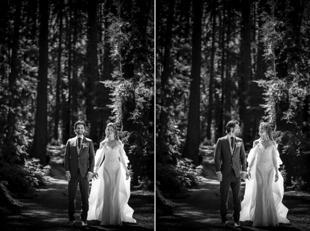 A bride and groom stand in a forested area at their Nestldown wedding, holding hands. Both are smiling and dressed in formal wedding attire.