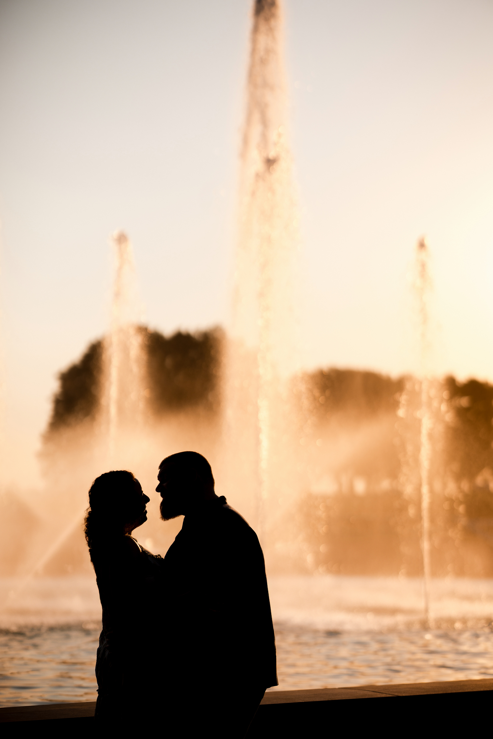 Silhouetted couple facing each other, backlit by a sunset with fountains in the background during a Longwood Gardens engagement session.