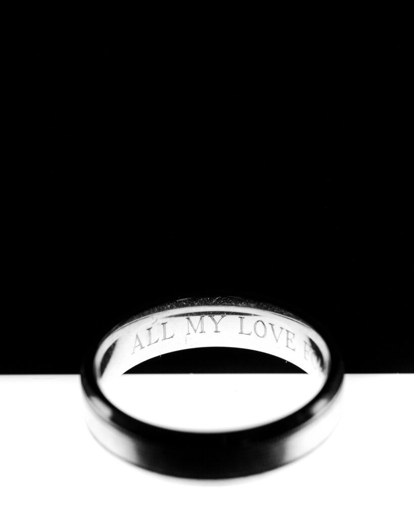 A close-up of a ring with the inscription "ALL MY LOVE" on the inner surface, set against a contrasting black and white background.