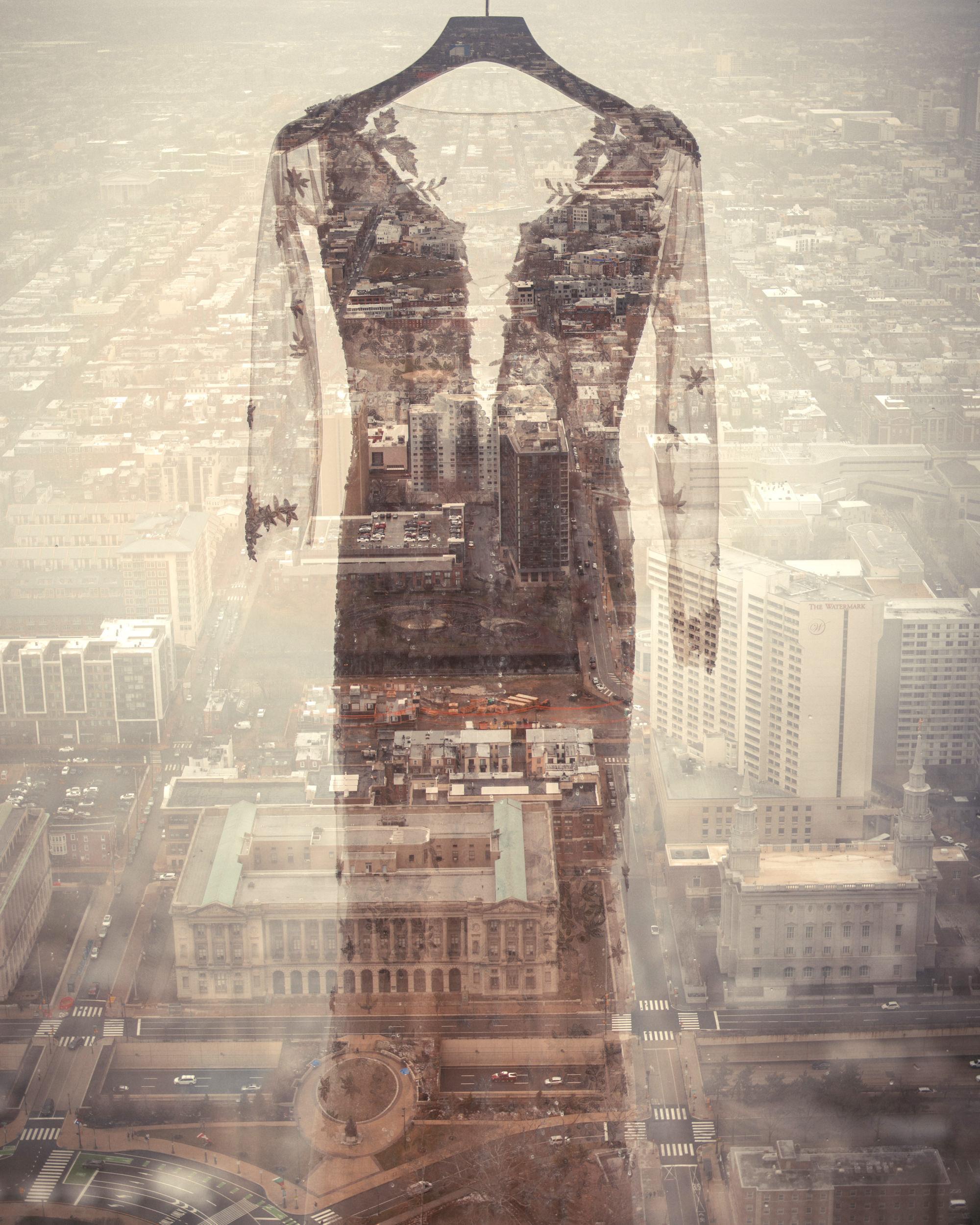 A sheer black lace dress is superimposed over a cityscape seen from a high vantage point, creating a double exposure effect.