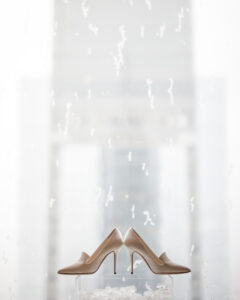 A pair of beige high-heeled shoes are displayed on a translucent platform with a blurred background.