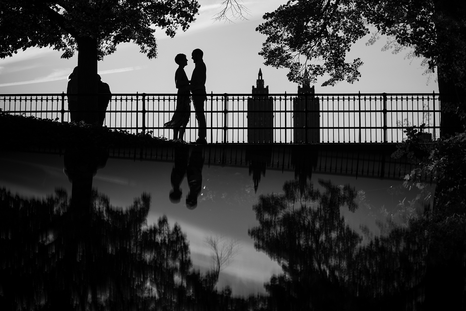 Silhouetted couple embraces on a bridge with city buildings in the ...