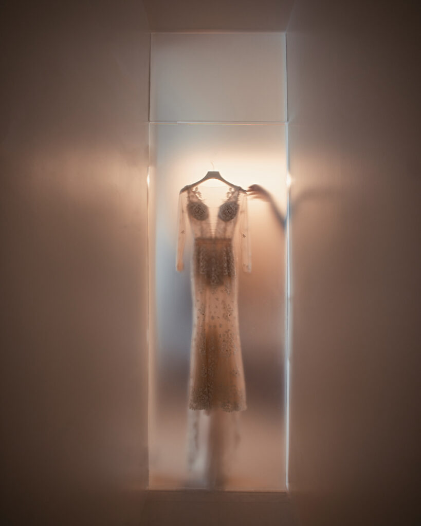 A long-sleeved, embellished dress hangs on a hanger in a softly lit space.