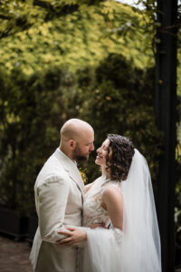 The bride and groom share an intimate moment, standing closely and gazing into each other's eyes with smiles.