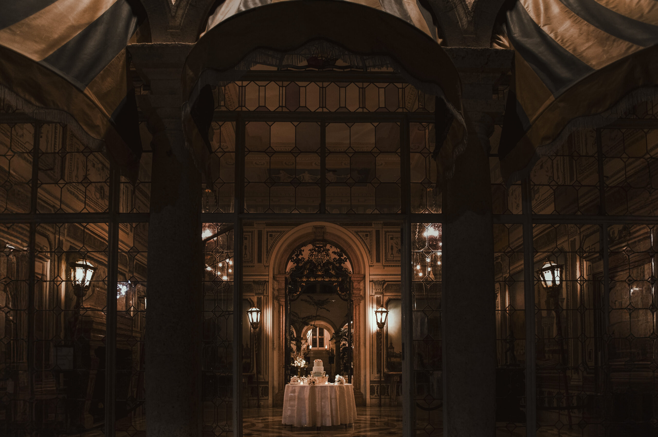 A cake is framed by an arch in a giant, empty room during a luxury wedding