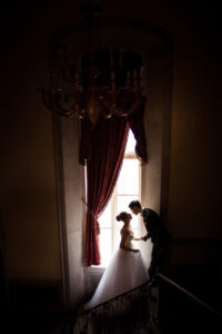 A couple leans in for a kiss with the light of a window frame illuminating them.