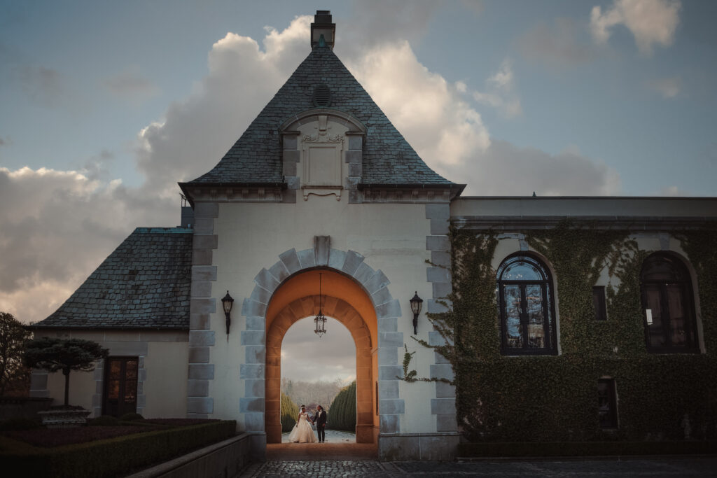 A couple on their wedding day stands under an arched walkway.