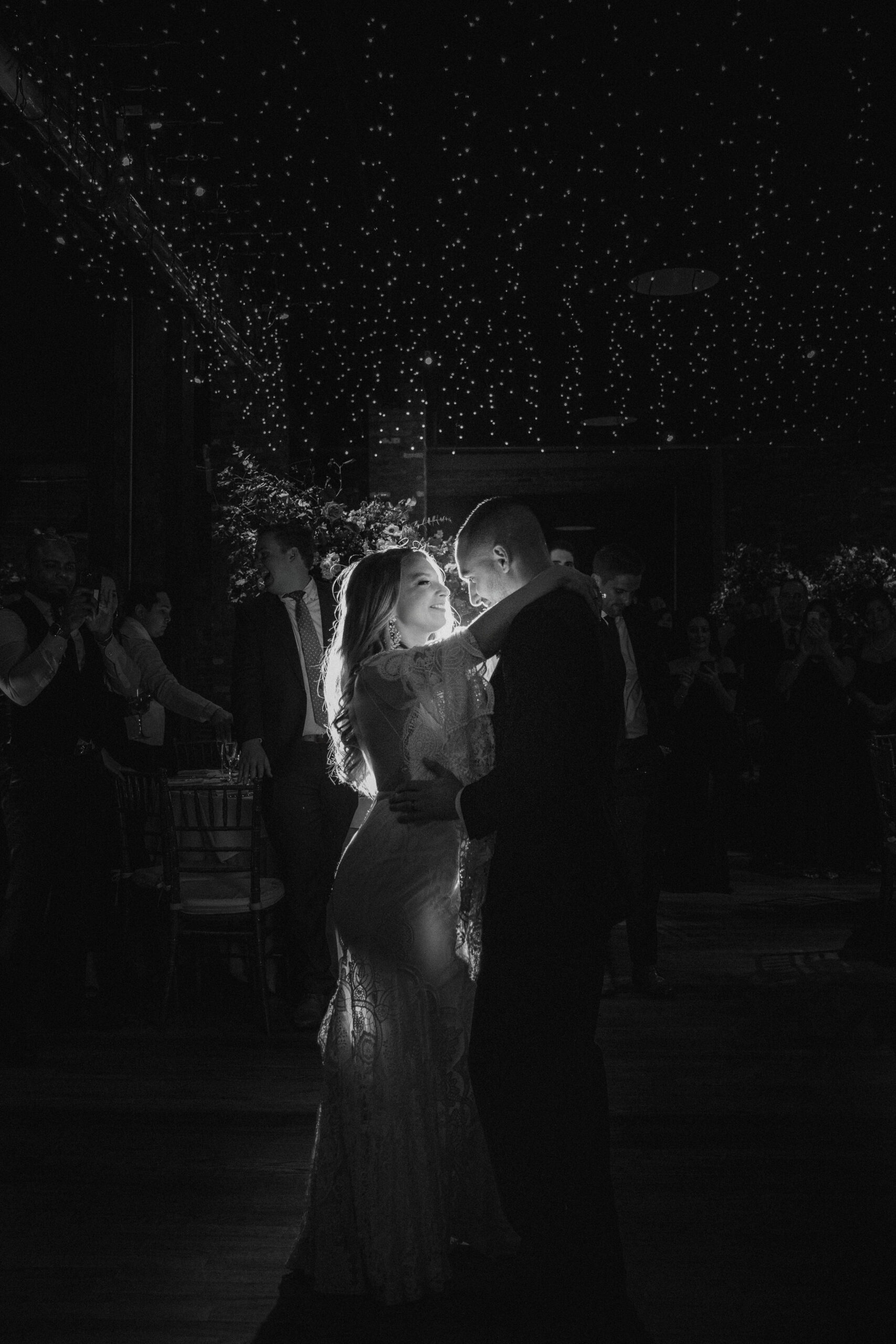 A couple shares a moment dancing on their wedding day, a light illuminating their faces.