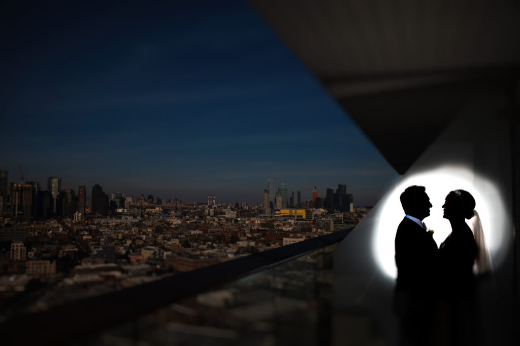 A couple is spotlit with a city in the background.