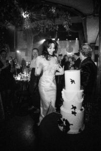 A bride stands in front of her cake with an excited face.