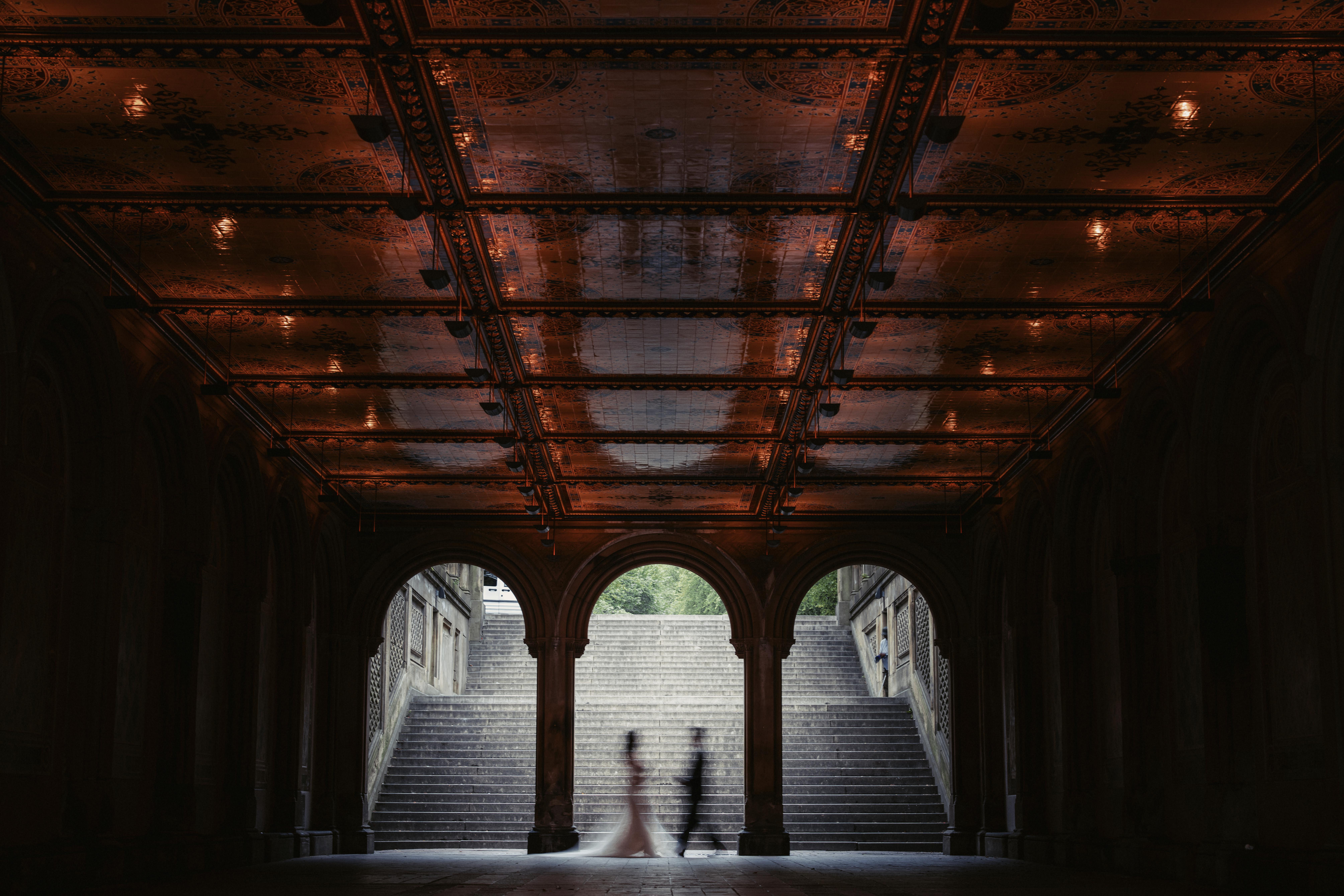 A silhouetted couple walks through an ornate, arched passage with a decorated ceiling and stone steps in the background, perfectly capturing the romance of boutique wedding photography in NYC.