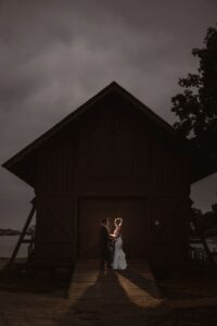 A couple stands in front of a dark, wooden structure, at Mystic CT wedding venues.