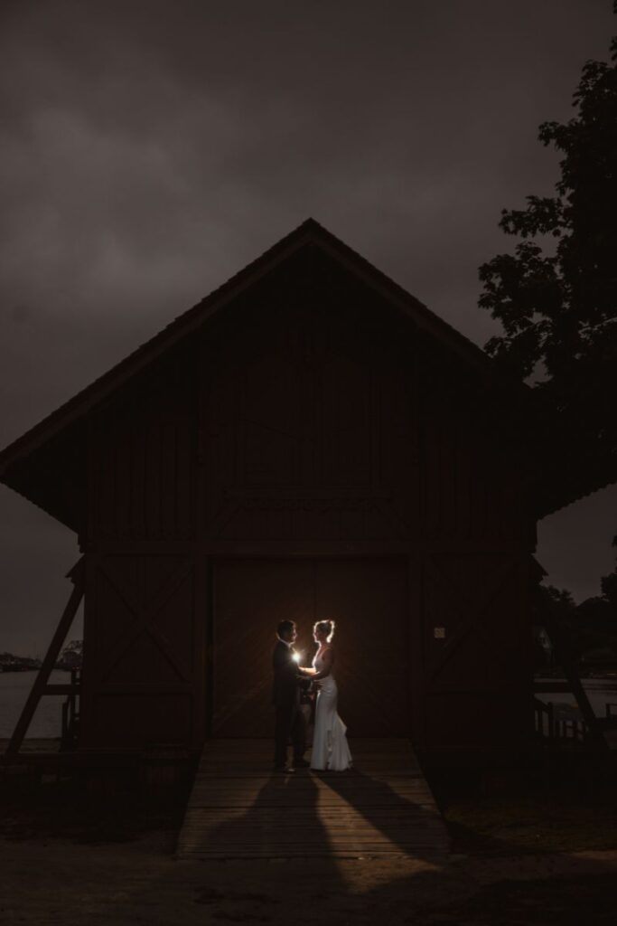 A couple stands outside a dark wooden building at night