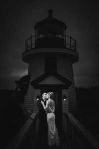 A couple shares a moment in front of a lighthouse at night, in Mystic CT's dreamy wedding venues.