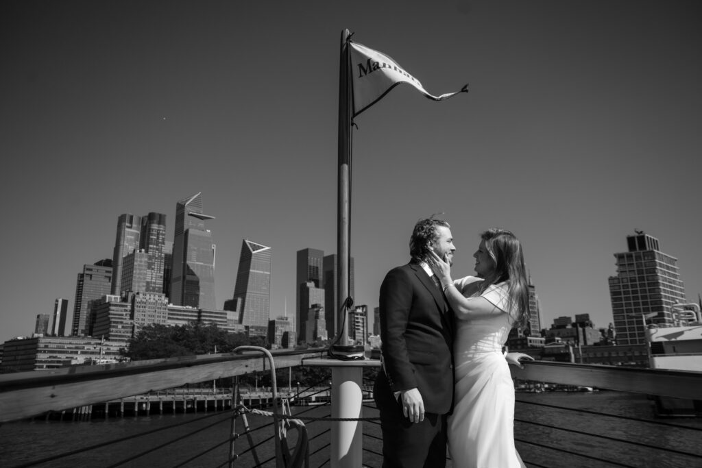 A couple in wedding attire stands on a boat, celebrating their NYC boat wedding with the stunning city skyline as a backdrop.