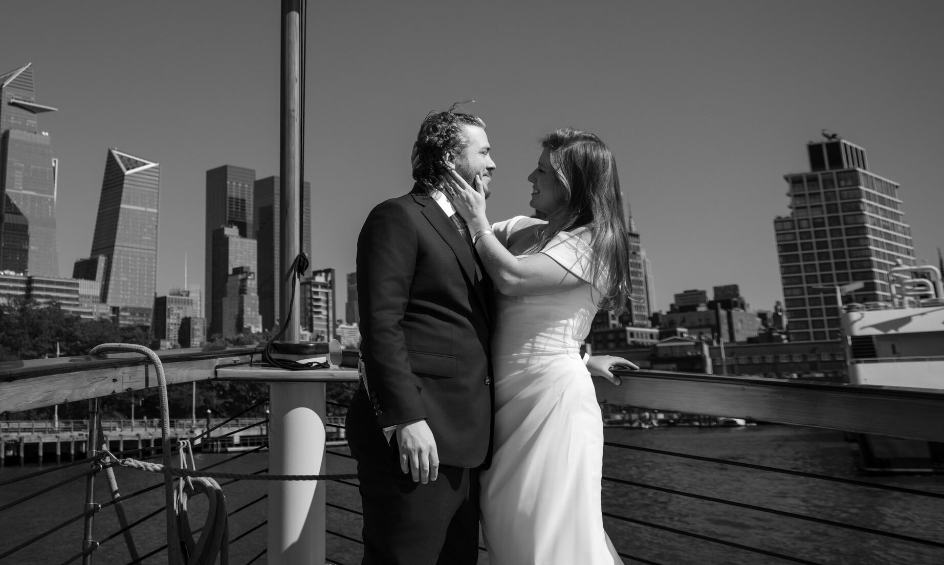 A couple in wedding attire stands on a boat, celebrating their NYC boat wedding with the stunning city skyline as a backdrop.