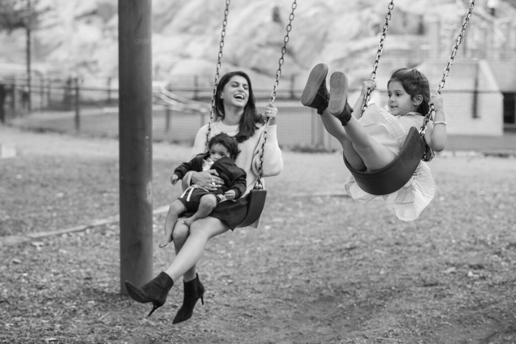 A woman swings with two children on a playground in Central Park. One child is seated on her lap, while the other swings beside her, capturing the essence of joyful family moments perfect for cherished photos.