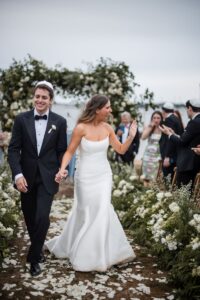 man and woman walking down the aisle at the wedding as their guest cheer for them the woman is in a white wedding dress and the man is wearing a black suit