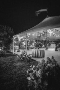 a tent with twinkling lights and tables covered with a cloth and a dance floor there are also flowers and other plants on display