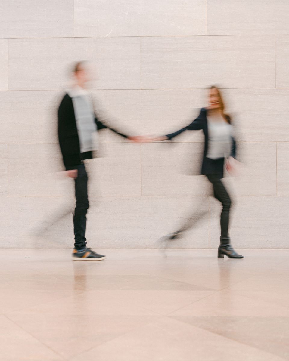 A couple running through a hall they are blurred and holding hands as they move foward