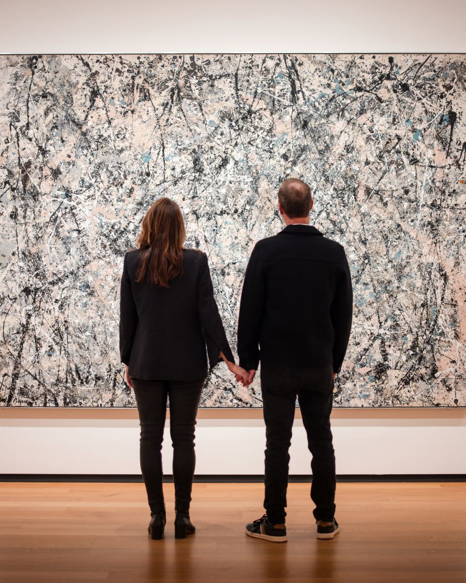 A couple looking at a painting holding hands they are both wearing black