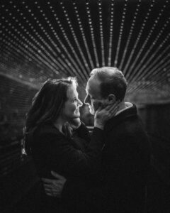 A couple looking into each other's eyes the woman has her hand on her partner's face and there are LED lights behind them