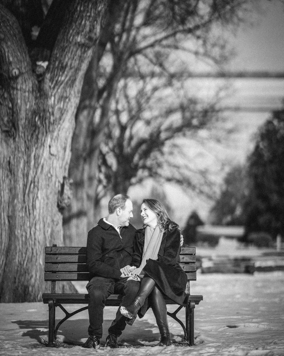 A couple sitting ona park bench holding hands and looking into each other's eyes