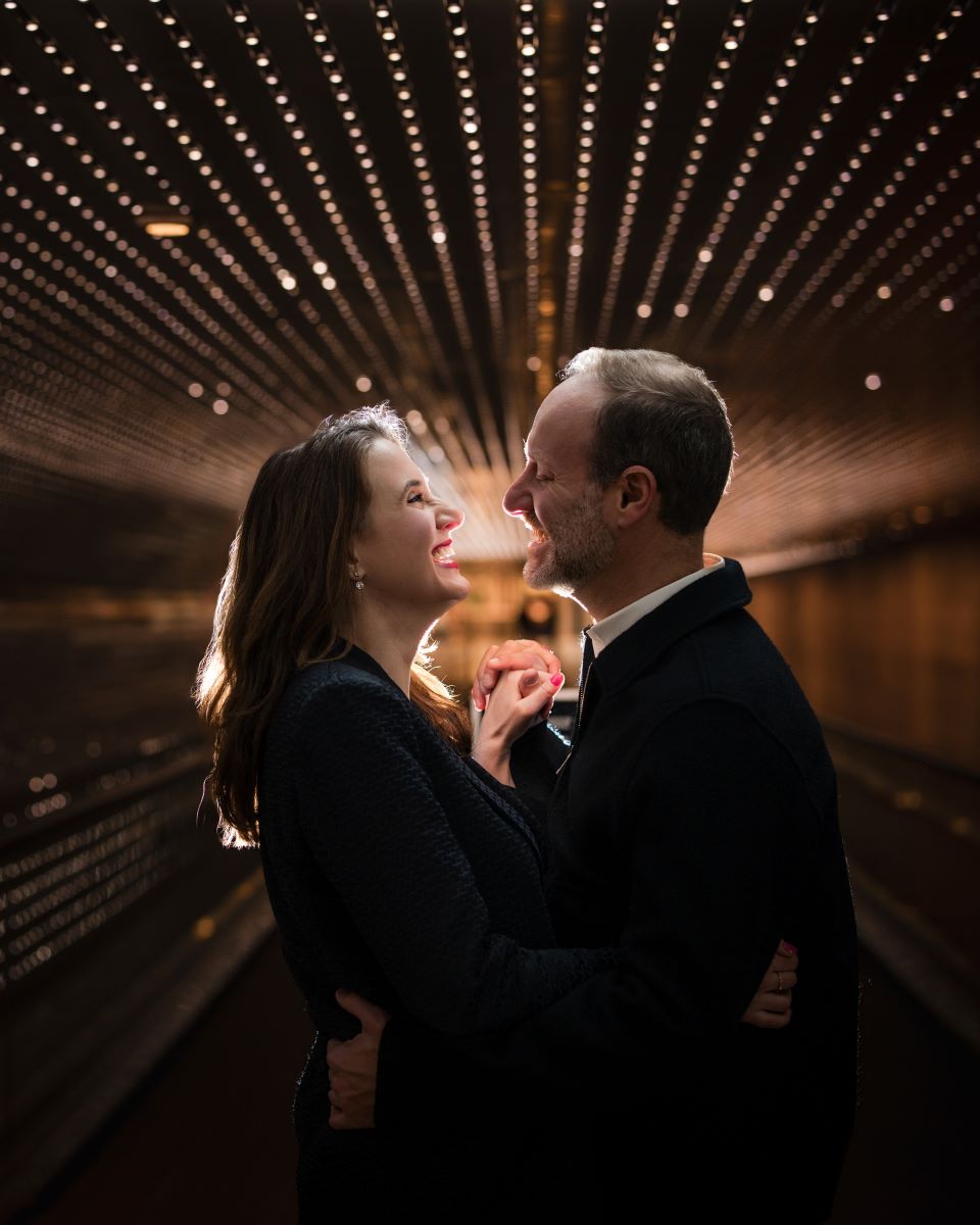 A couple looking into each other's eyes laughing and holding hands and embracing behind them are LED lights 