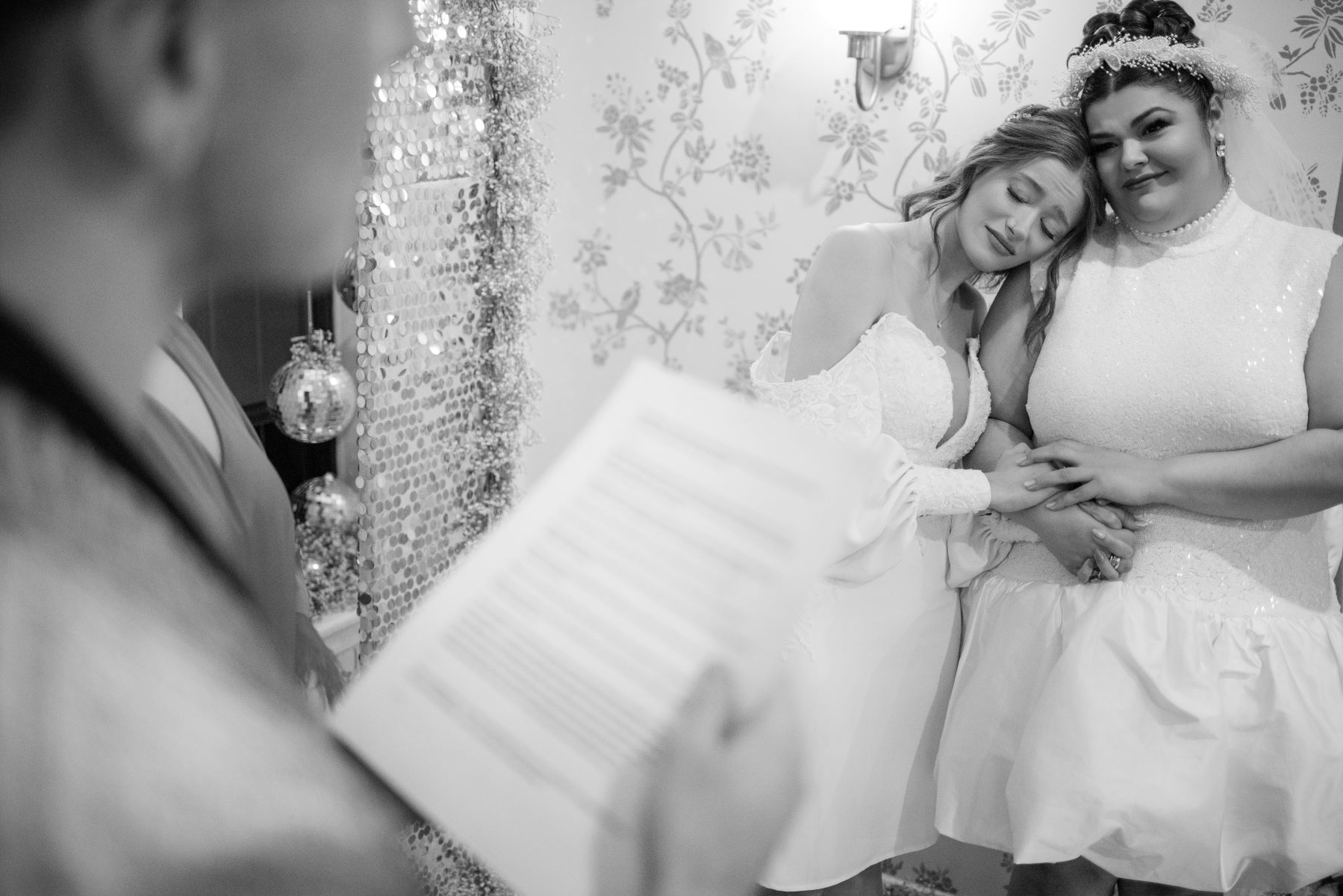 two women at their wedding ceremony in their home holding hands while their officiant stands in front of them