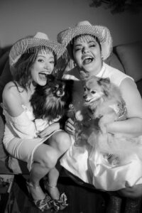 two women wearing cowgirl hats and their wedding dresses and holding their dogs