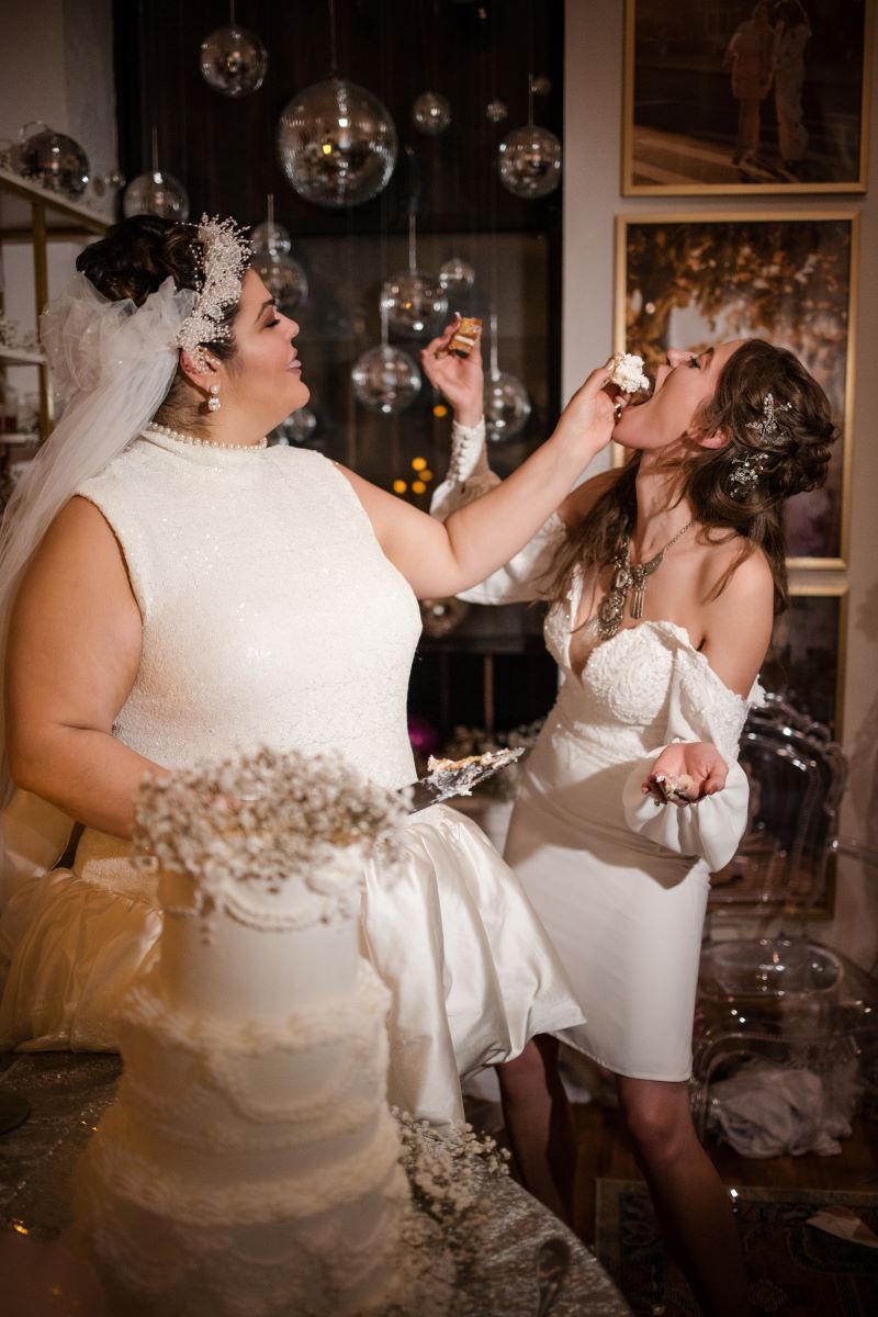 two women celebrating their wedding at home one woman is feeding the other woman a piece of their wedding cake