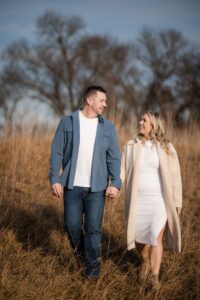 A man and woman holding hands and strolling through a grassy field in Doylestown's scenic terrain, with trees in the background. They're dressed in casual clothing.