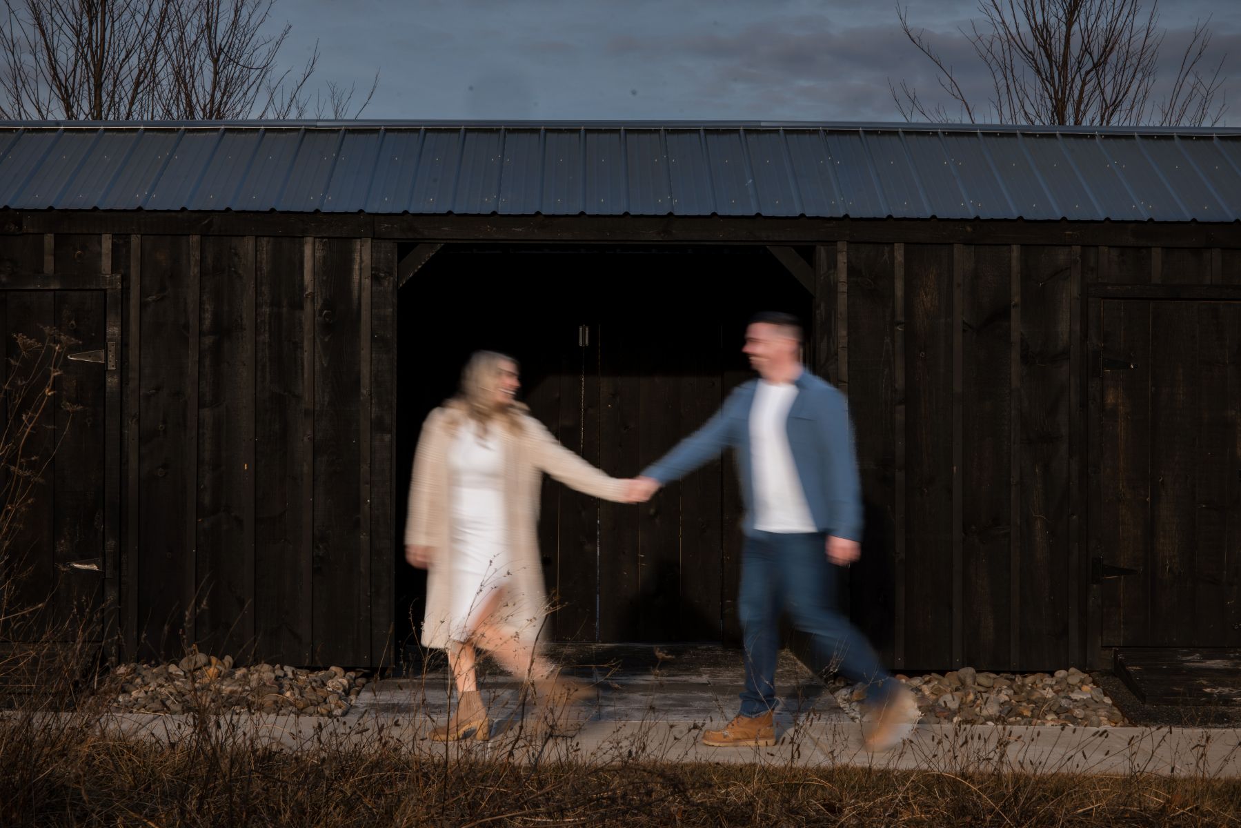 a couple walking together in front of a barn like structure and holding hands the two people in the images are blurred to create movement