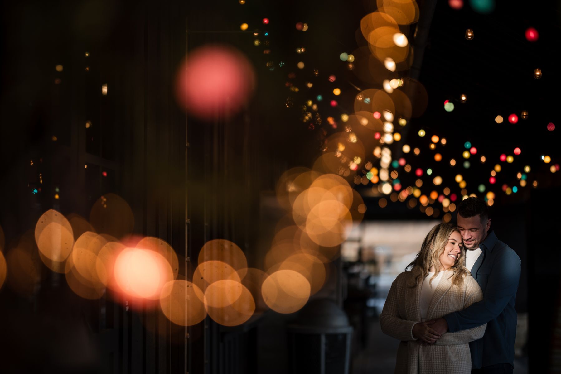 a couple standing together hugging one another and behind them are twinkling lights