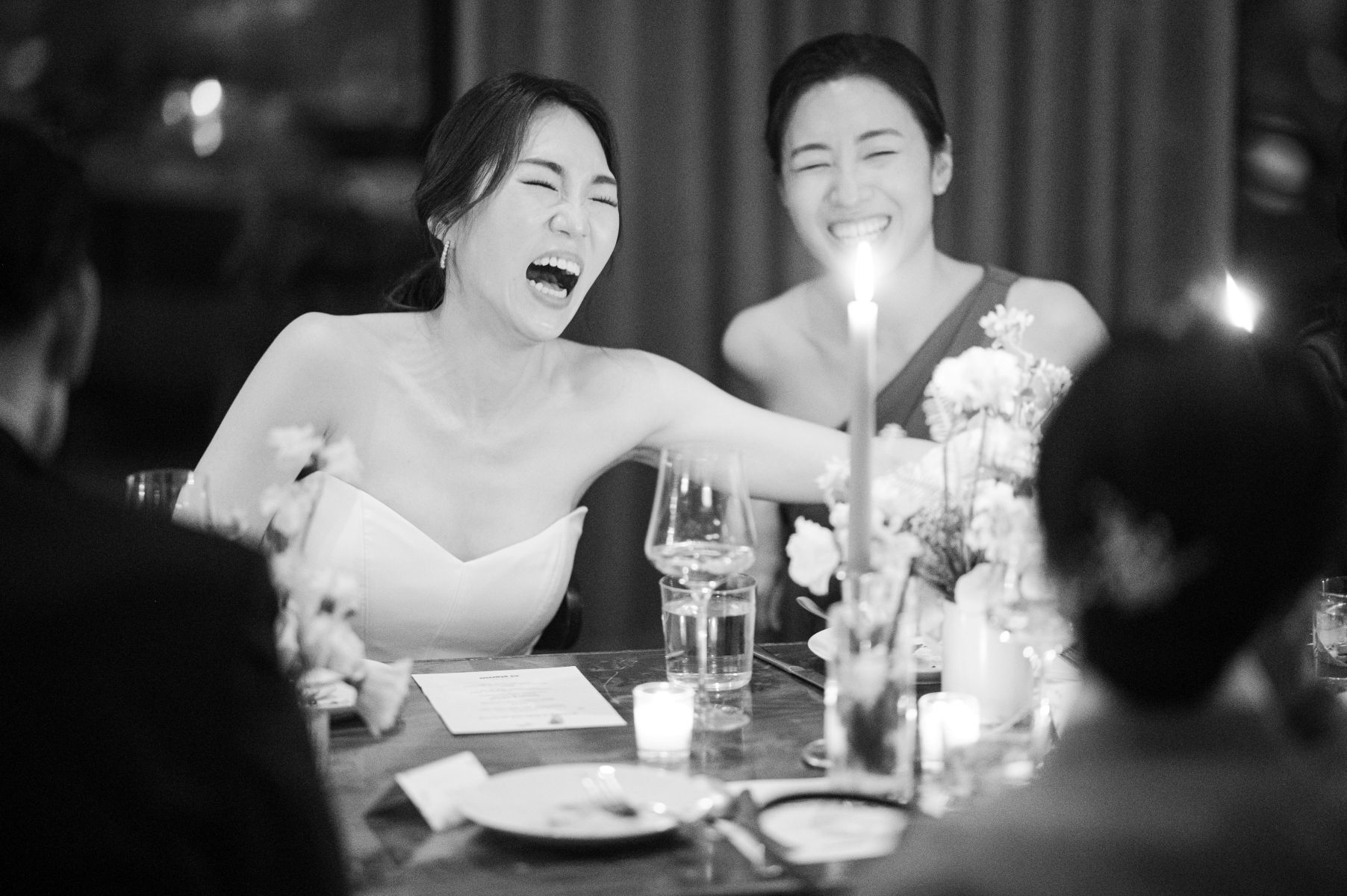 a woman in a white wedding dress laughing with her wedding guests while seated at a table