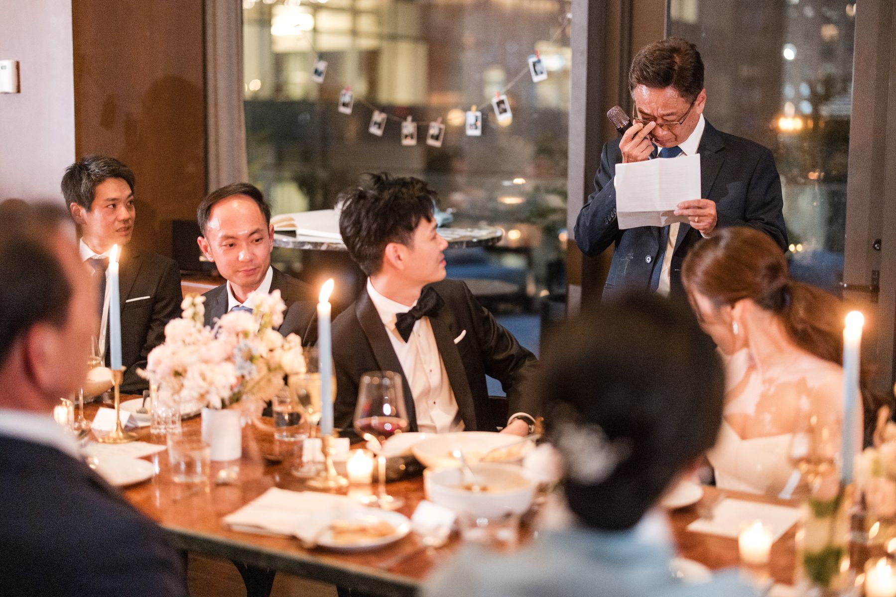 a man reading a speech at a wedding reception he is wiping a tear from his eye 