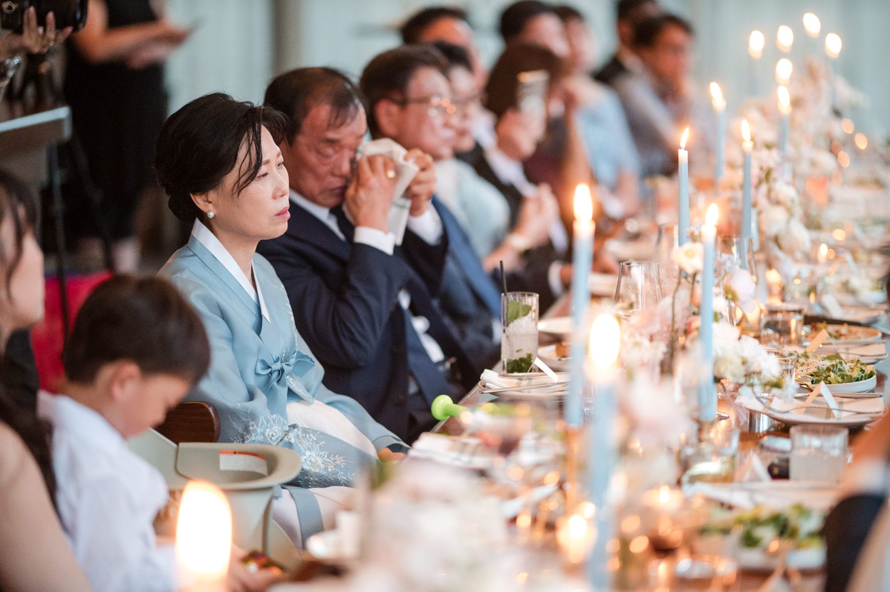 a group of people sitting at an elegantly decorated dining table adorned with candles, floral arrangments, plates, and napkins