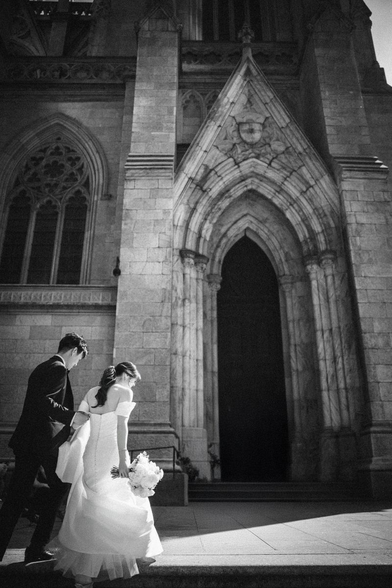 A bride and groom walk up steps toward the entrance of st patrick's cathedral in new york
