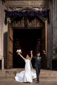 A bride and groom celebrate as they exit a cathedral