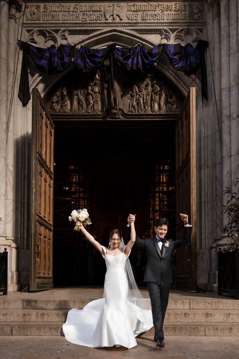 A bride and groom celebrate as they exit a cathedral