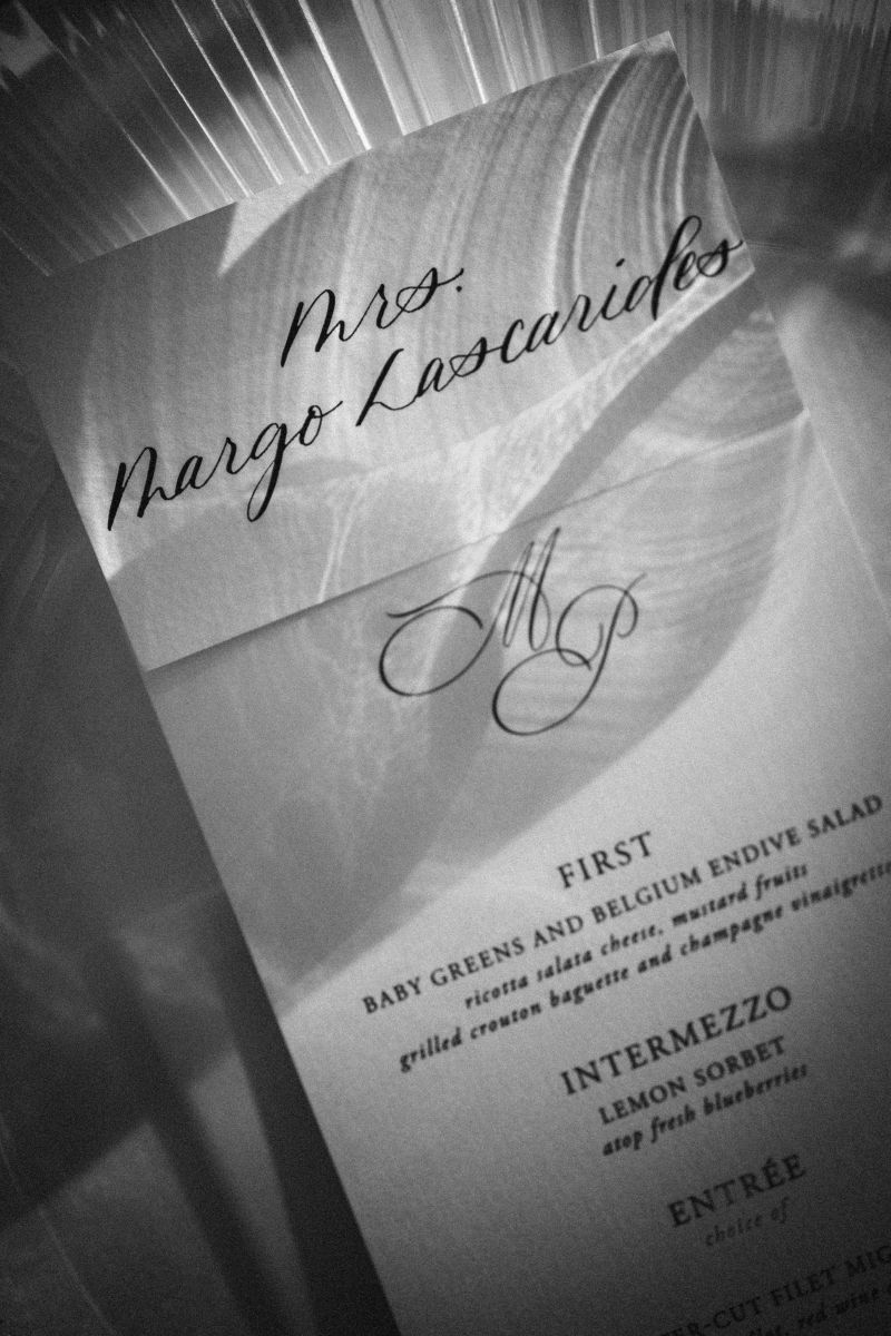 A formal dinner menu and place card labeled "Mrs. Margo Lascarides" displayed on a glass plate, styled elegantly for a wedding at The Grand Belle in Philadelphia.