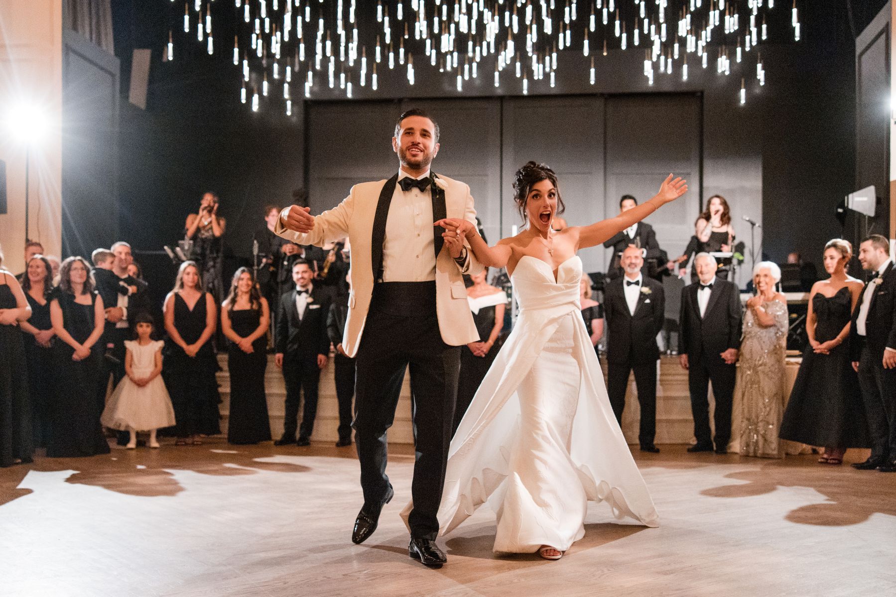 a couple holding hands and making an entrance at their wedding reception while surrounded by their guests