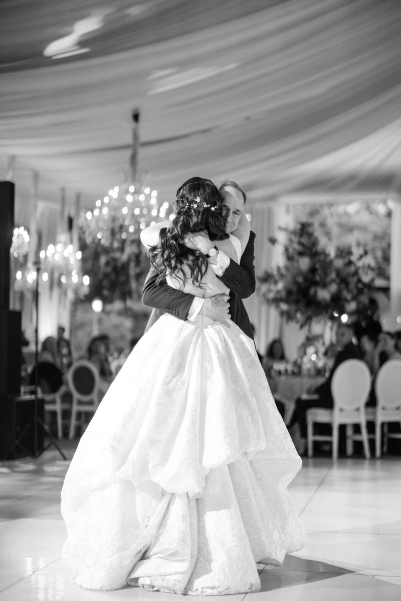 A bride with her father shares a close embrace while dancing in a beautifully decorated ballroom at their wedding reception