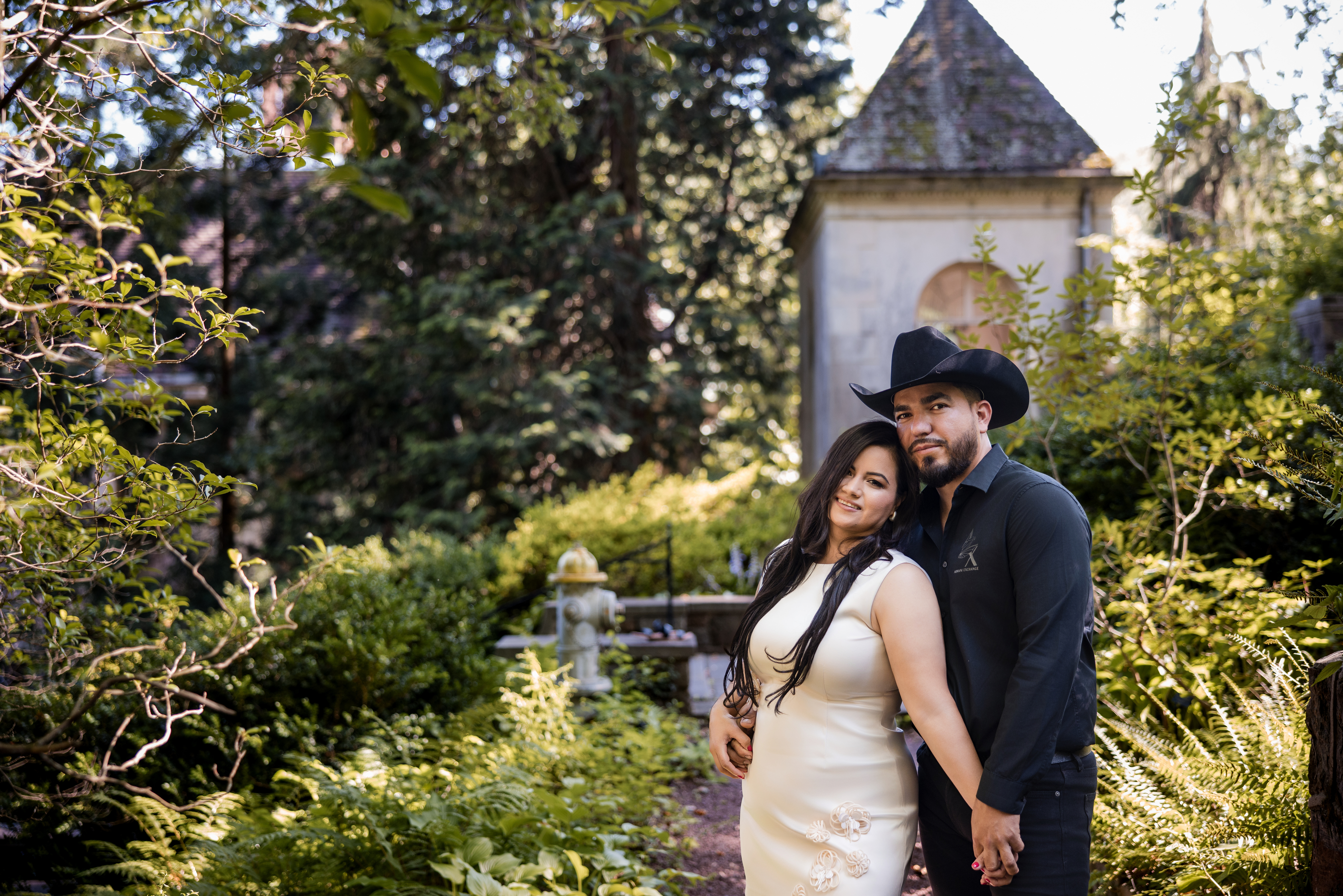 Engaged couple posing in front of a historic garden pavilion at Winterthur Museum in Delaware, surrounded by lush greenery and summer foliage during their engagement session. Ask ChatGPT 