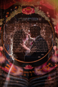 A bride and groom stand facing each other, backlit, with a floral, Hebrew-inscribed marriage contract (ketubah) superimposed over them at their unforgettable Angel Orensanz Wedding.