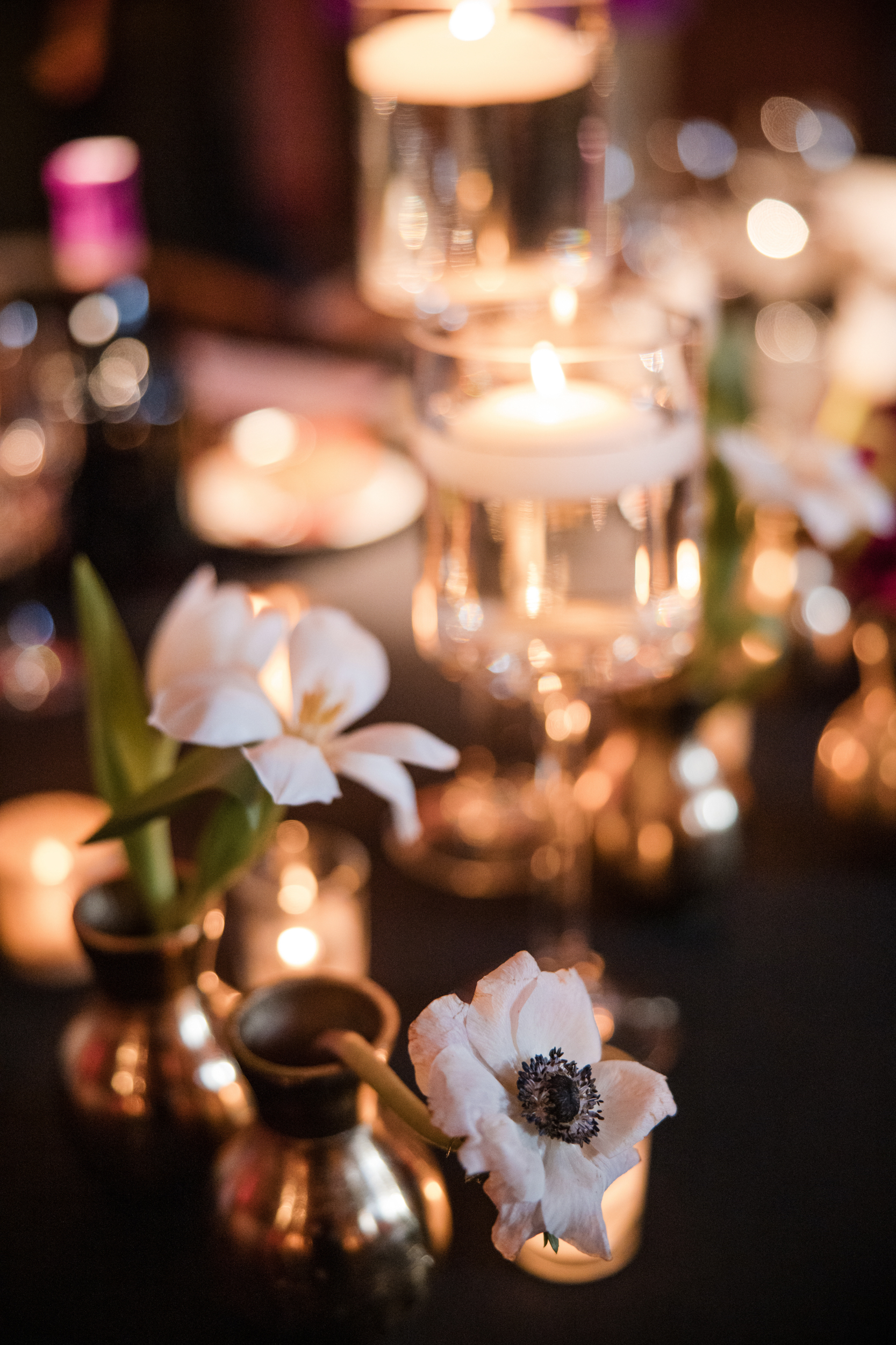 A close-up of white flowers in small vases and floating candles in glass holders on a dimly lit table, capturing the romantic ambiance of an Angel Orensanz Wedding.